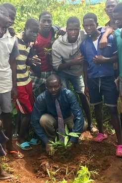 A group of Malawian students and their teacher stand around a newly planted bamboo seedling