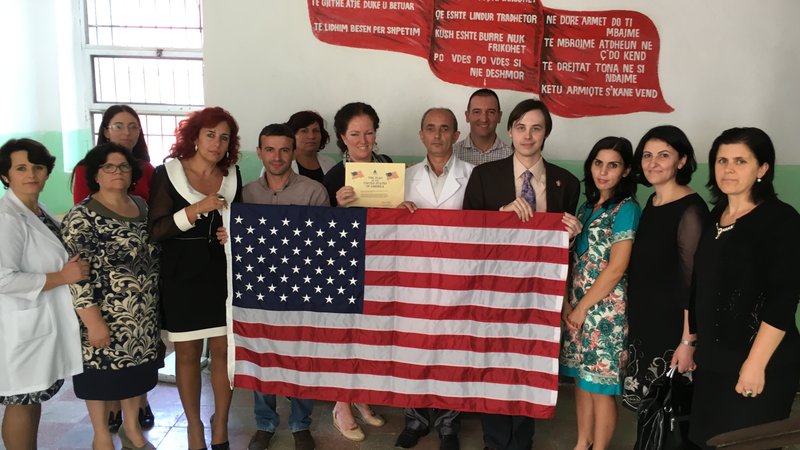 A group of people stand behind an American flag, smiling.