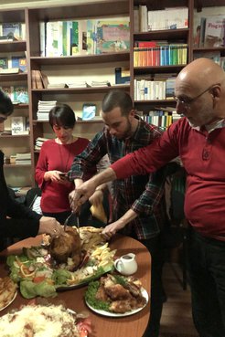 Two people serving themselves food in front of a bookshelf