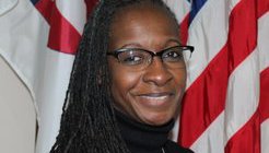 A Black woman smiles in front of an American flag for her professional head shot