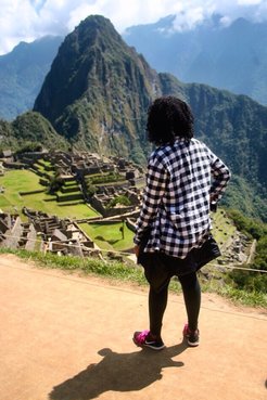 A Peace Corps Volunteer stands with her back to the camera. Machu Picchu, a bold mountain peak, is in the background.