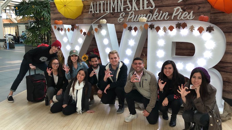A group of U of A students throw up their school sign in front of an airport.