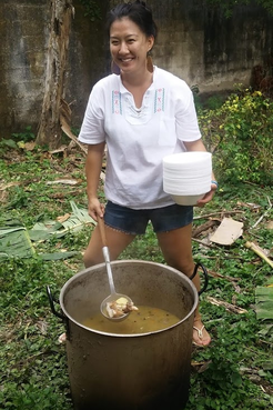 A Korean American woman stirs a big pot of soup outside