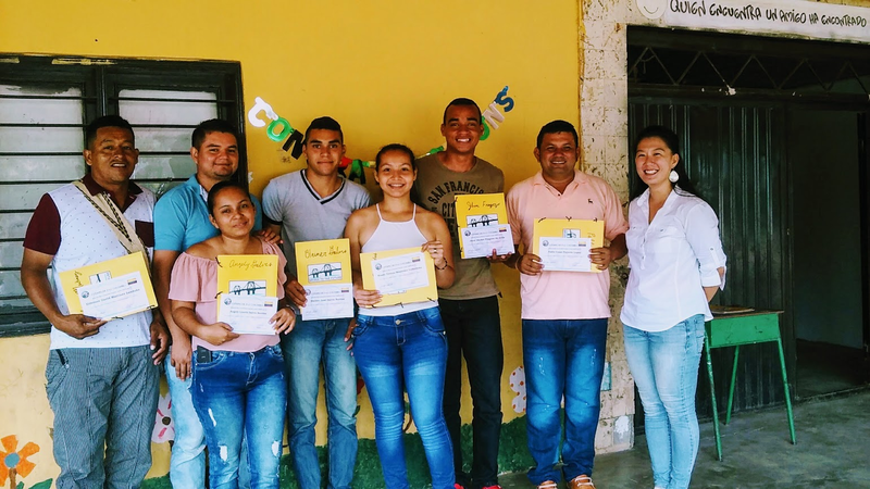 A group of people in Colombia stand outside smiling in front of a yellow wall.