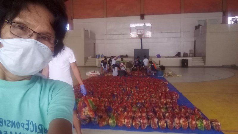 A woman wearing a mask stands in front of hundreds of bags of recently packed produce