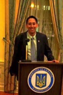 A white man stands at a podium, smiling.