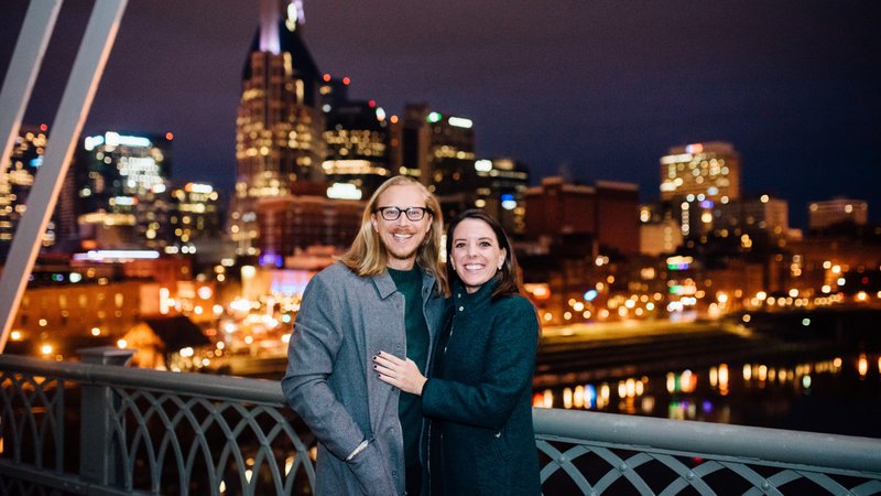 Two people stand in front of a nighttime city skyline.