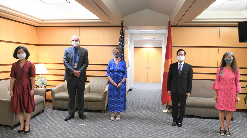 A group of Americans and Vietnamese folks stand inside in a socially distant line with masks on.