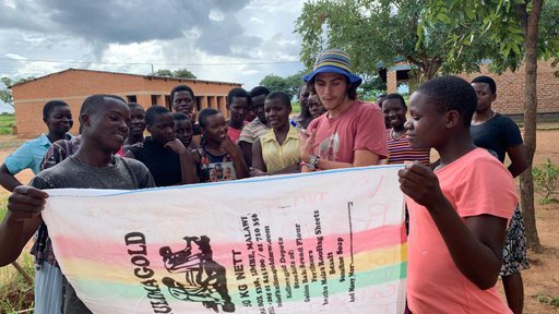 A group of people stand behind a maize sack sign with information written on it