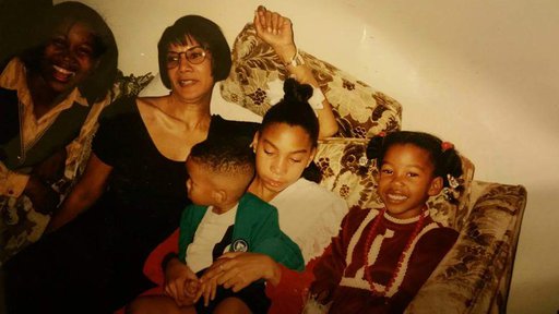A family of several people, young children and adults, all sitting on a couch inside.