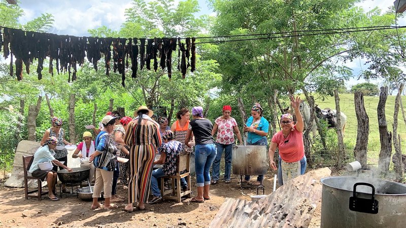 A group of Panamanians and a young white woman stand outside cooking in a big group, with smiles.