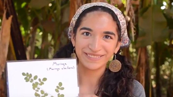 A female Volunteer holds a picture of moringa and smiles.