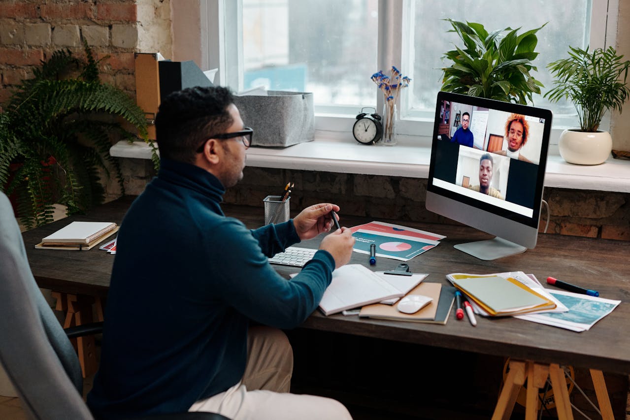 Professional taking notes while attending an online learning session with peers on a video call.