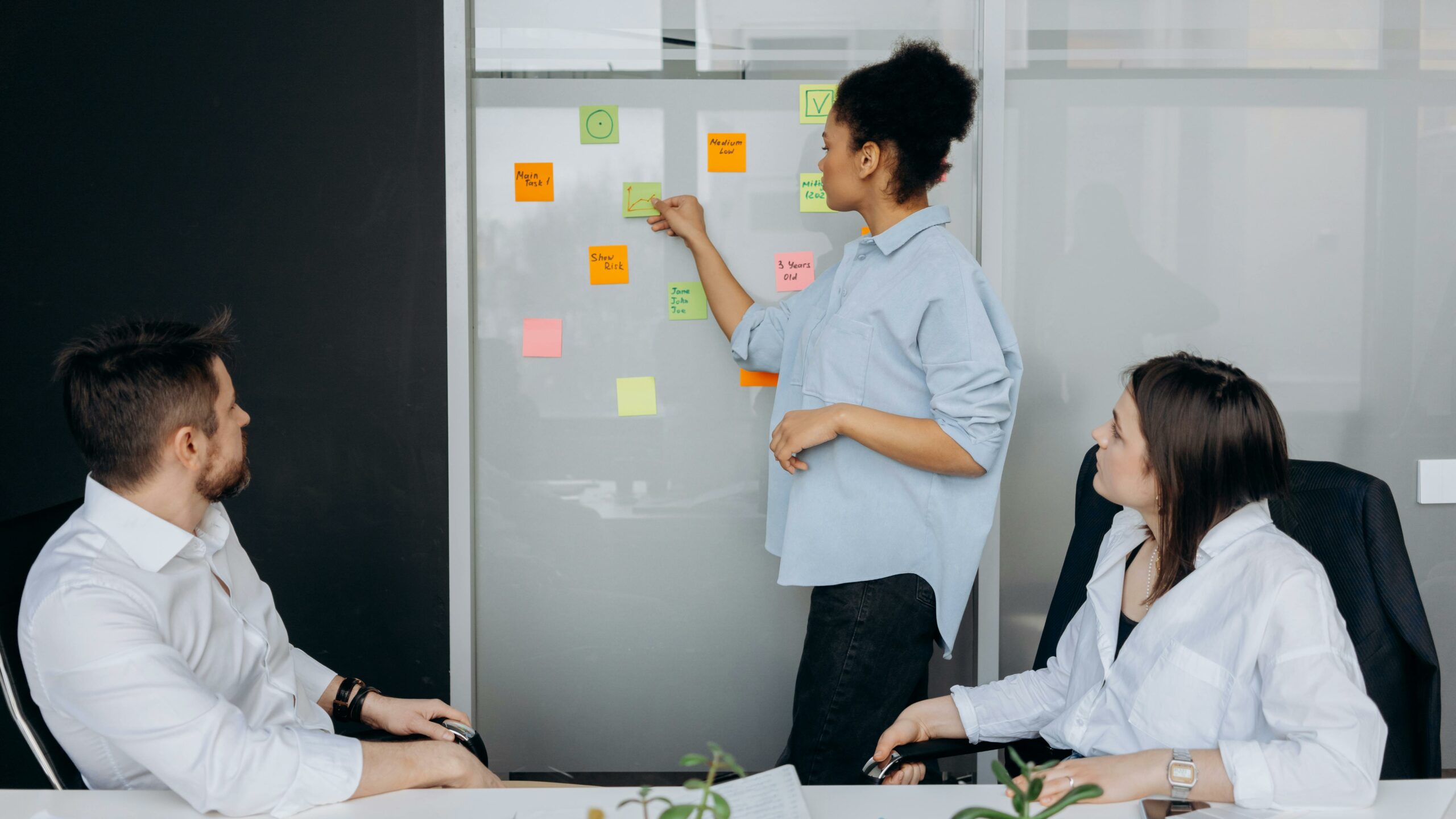Three colleagues in discussion while reviewing colorful sticky notes on a whiteboard, symbolizing how member feedback is collected and turned into strategy.