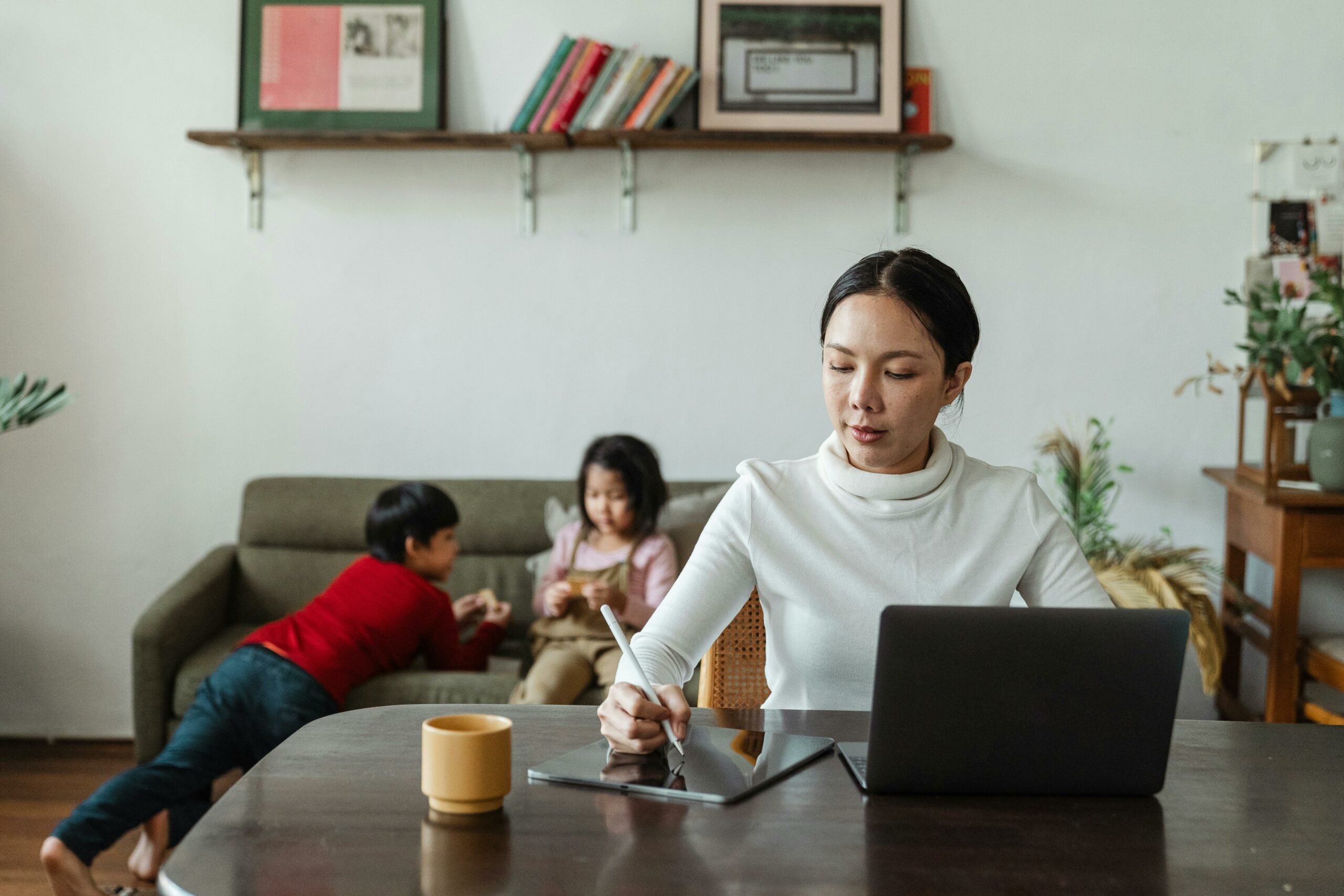Professional completing an online learning module on a laptop at home while children play nearby — representing flexible microlearning for busy association members.