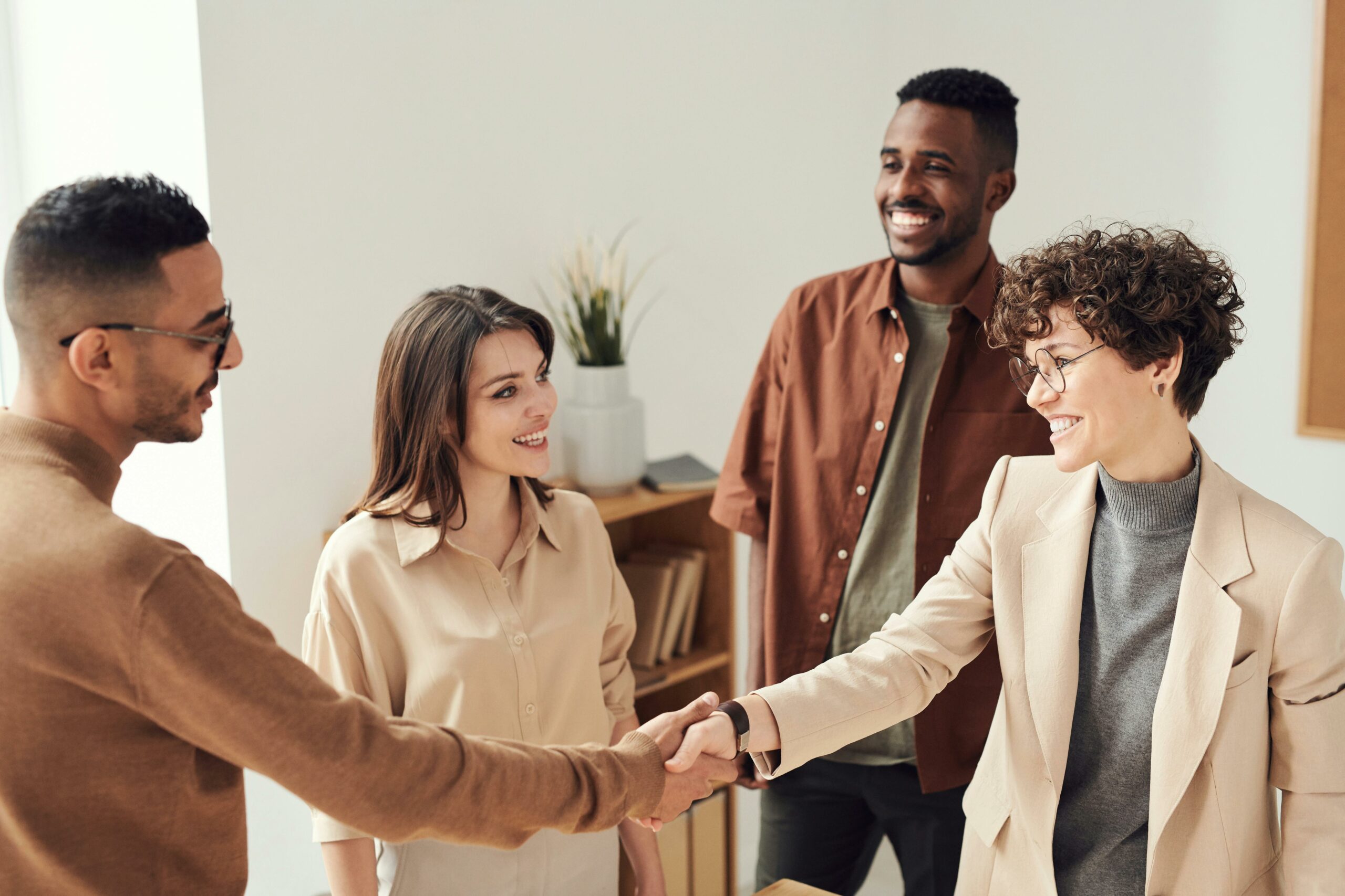 A man and woman are shaking hands. They are with one more man and woman, and talking about how to reduce member churn.