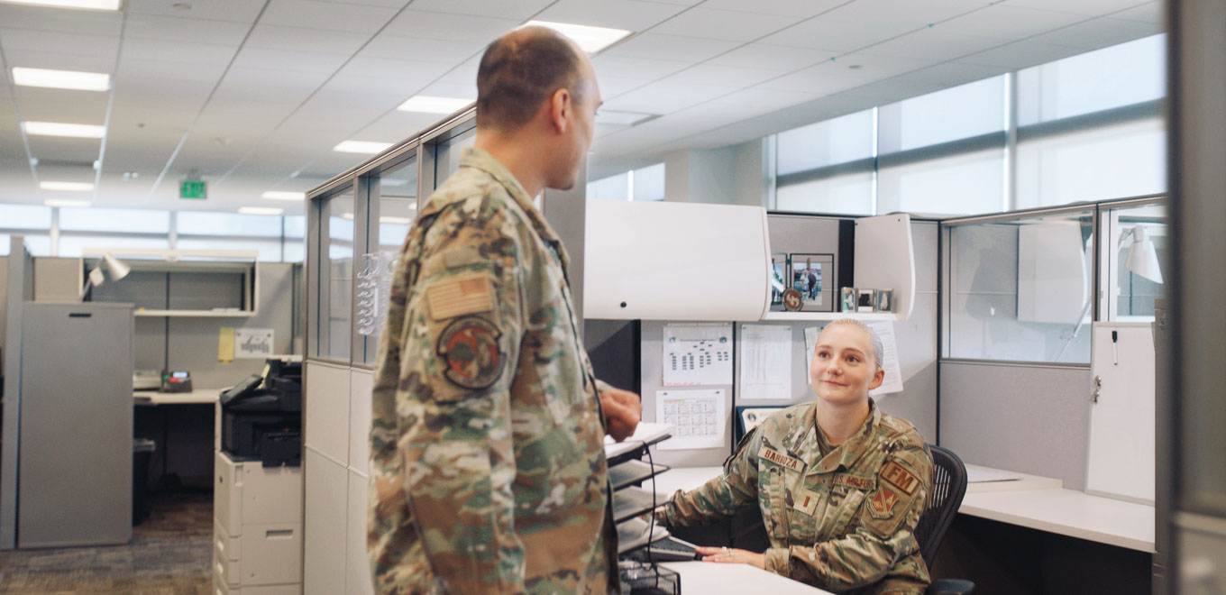 Hope speaks with a colleague while sitting at her desk