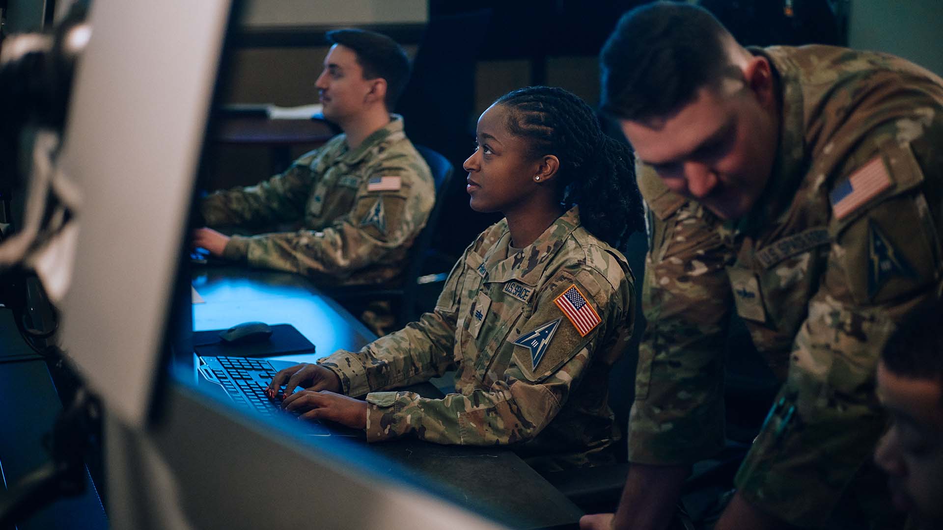 Syriah Harris working at her computer with 2 other service members