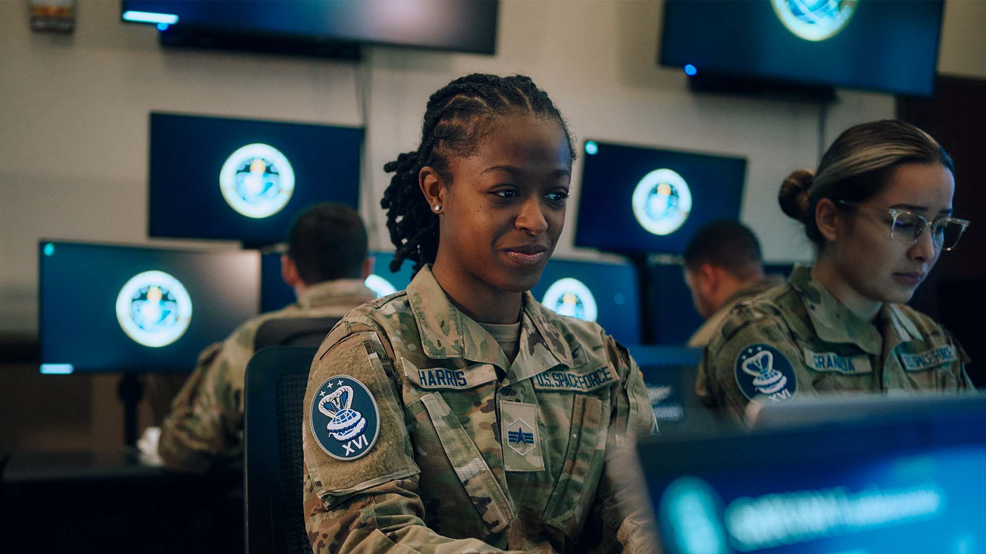 Syriah Harris working at her computer with 1 other service members
