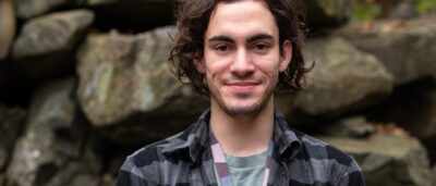 Image of man with dark hair and dark eyes standing in front of rocks