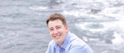 Image of man sitting on rock with water in background