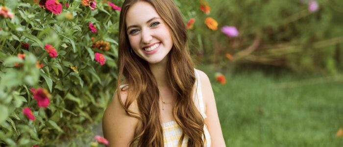 Woman with long hair sitting in grass, surrounded by flowers