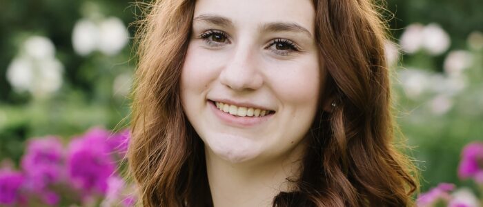 Smiling woman with long auburn hair and flowers in background