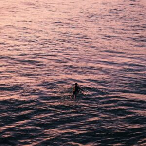 Person paddling out on a surf board on calm water at sunset