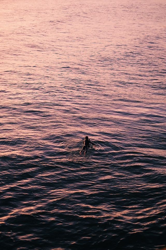 Person paddling out on a surf board on calm water at sunset