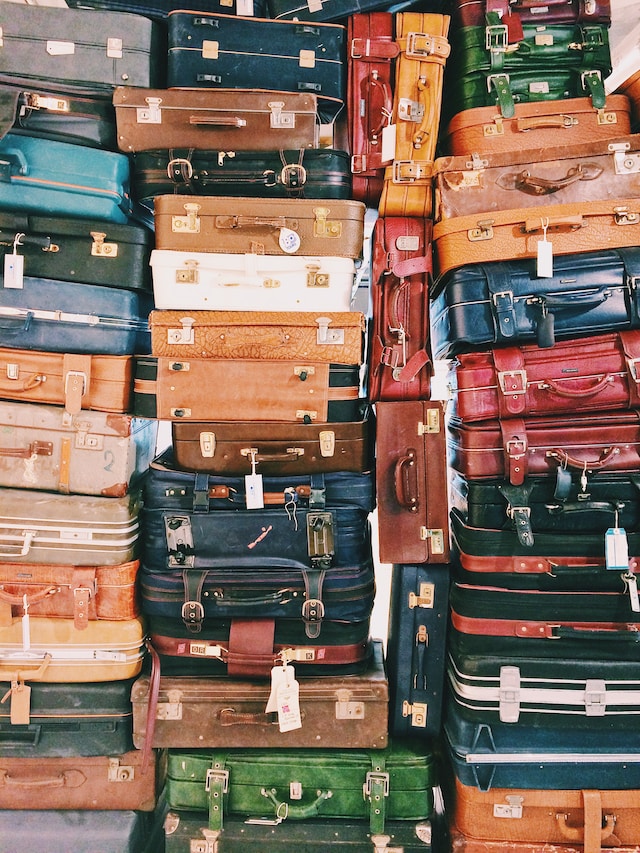30+ suitcases piled on one another, variety of sizes and colors