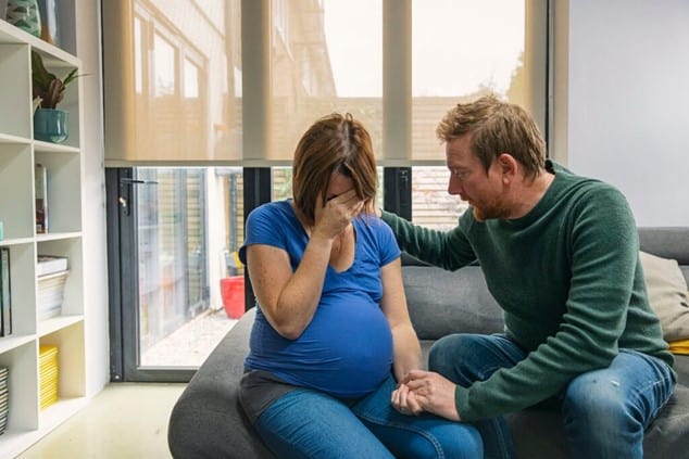 Pregnant woman crying, man comforting her