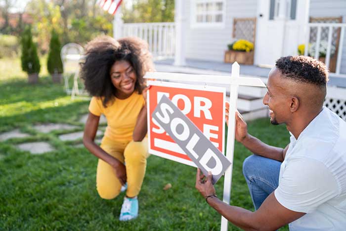 African American couple put a Sold sign on the For Sale sign in their front yard.
