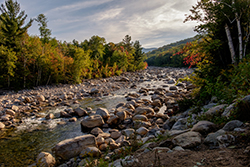A riverside image of a rocky river bed surrounded by trees in Enfield, NH