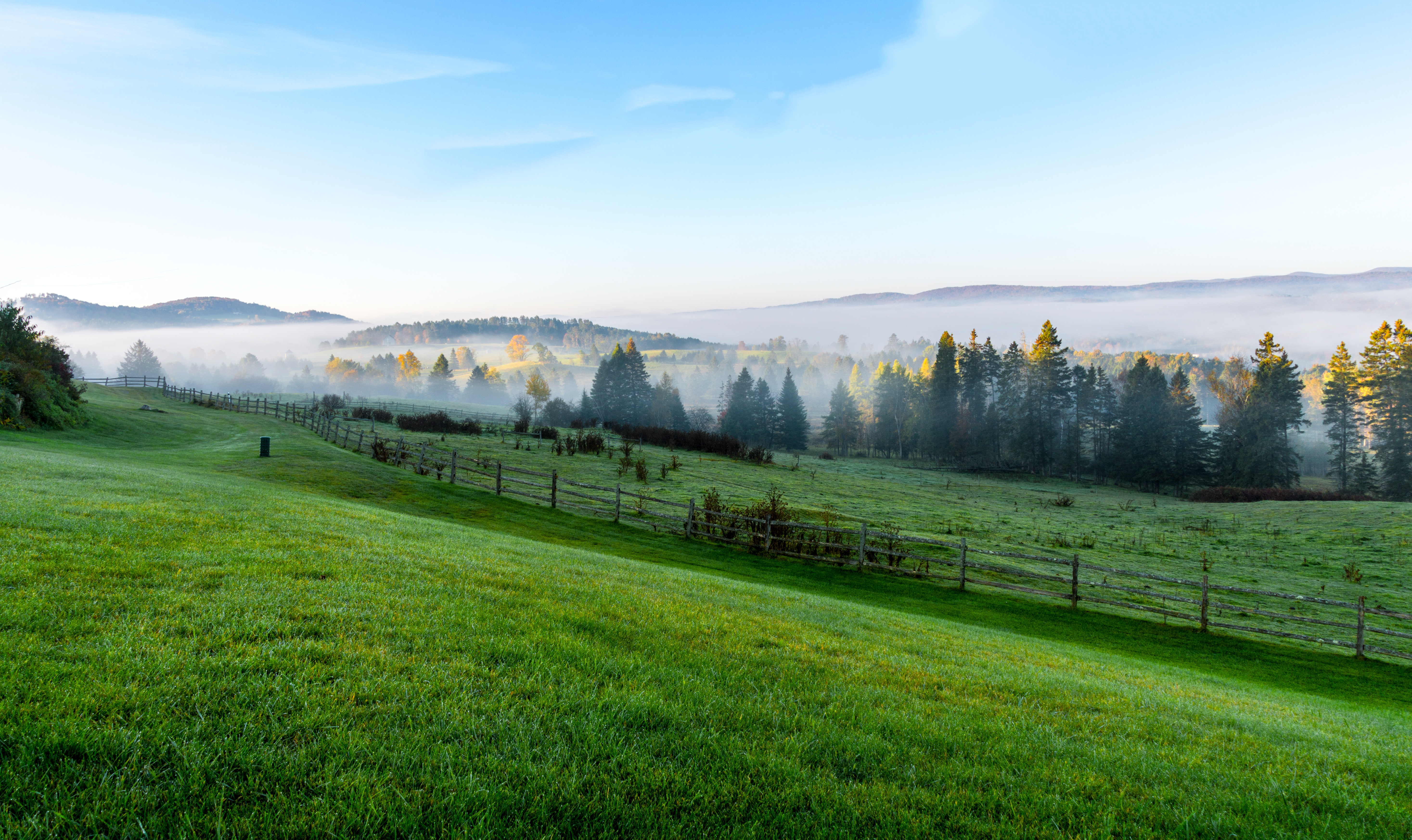 A scenic view of rolling hills and fenced farmland with mist-covered mountains in the background