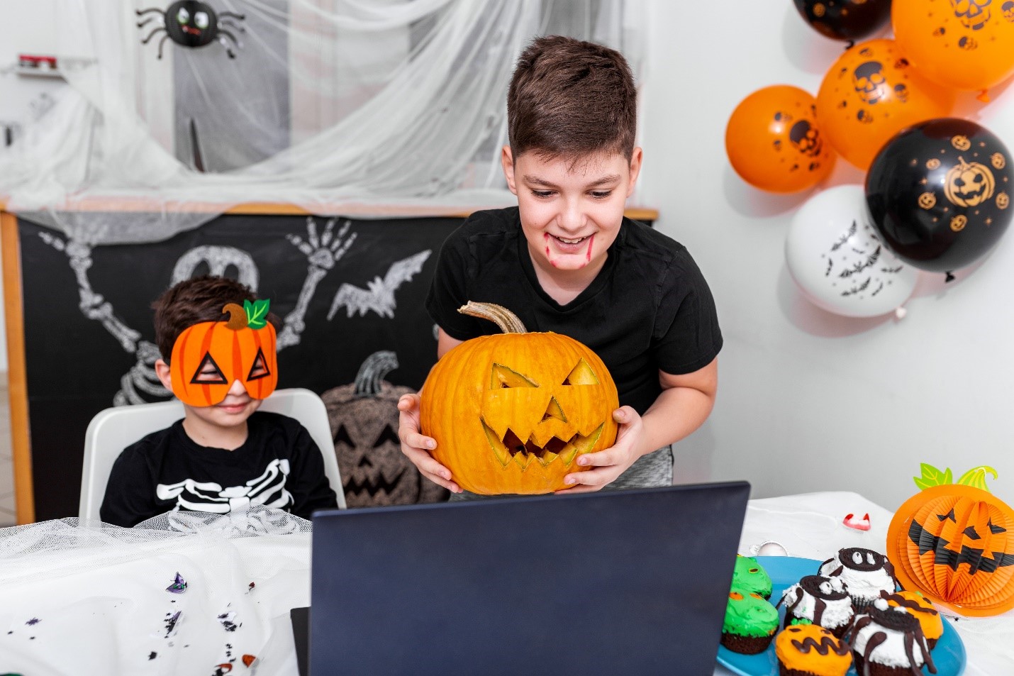 A boy with a laptop, smiling. Halloween decorations behind him.