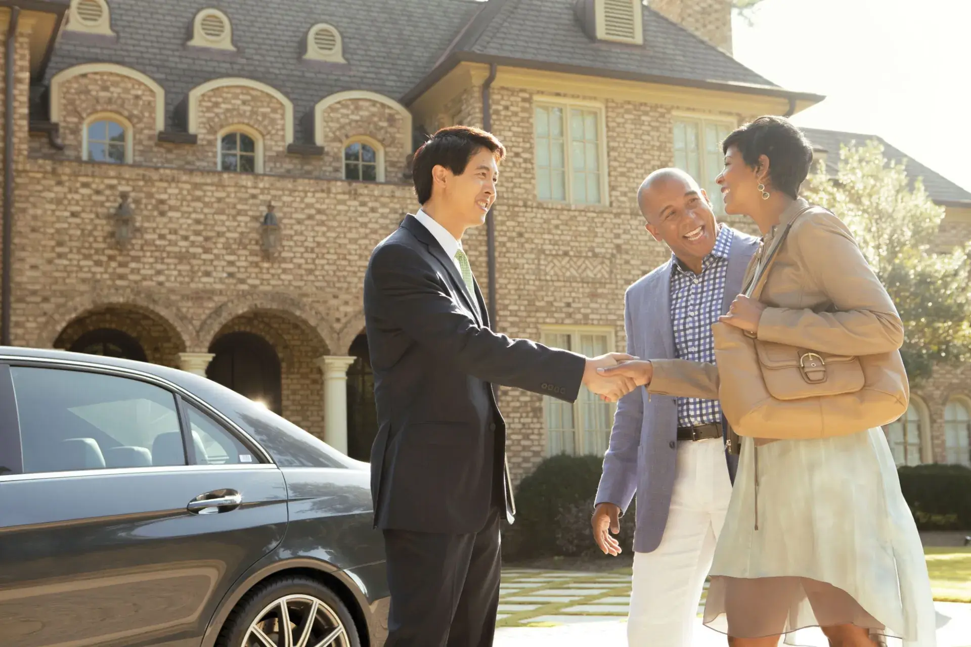 Couple shaking mans hand in driveway of luxury home