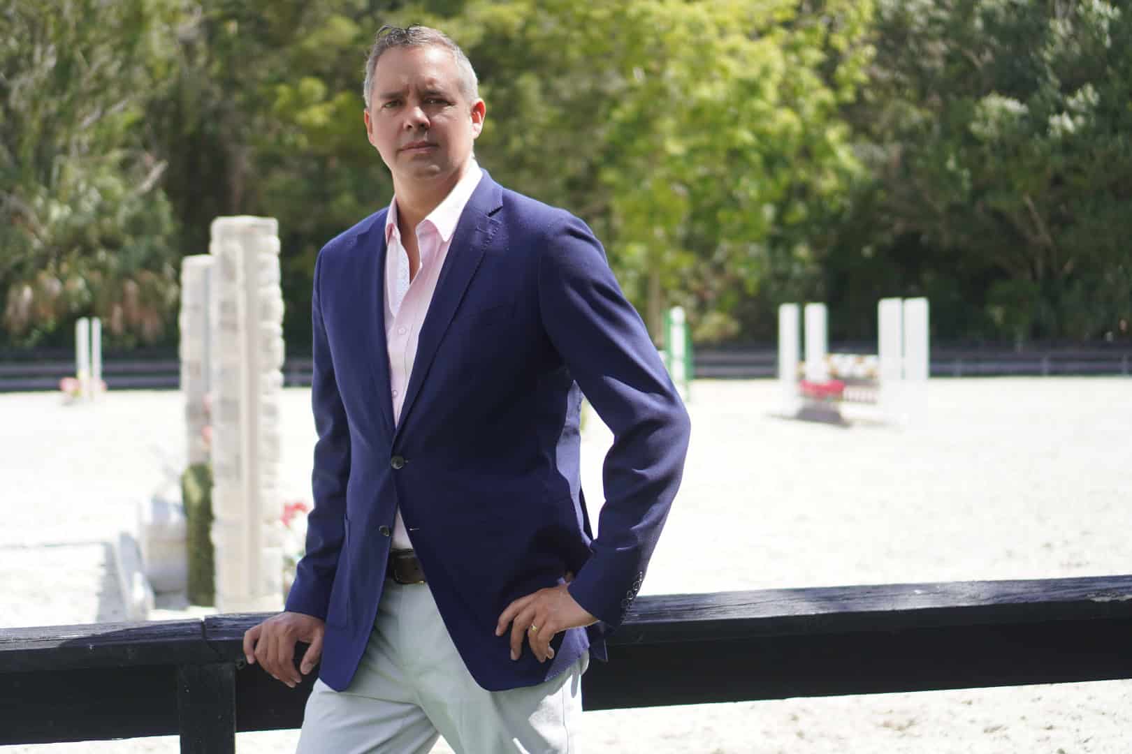 Matt Piccirilli real estate broker wearing an elegant blue suit outside with one hand on the rail of a horse jumping ring