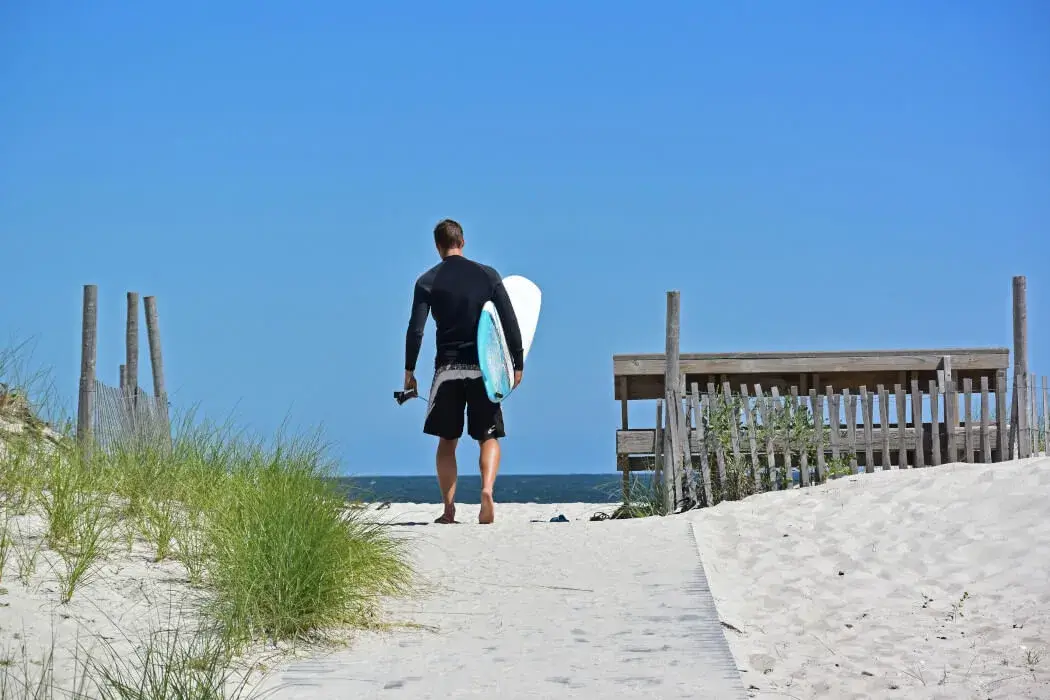 Man heading to the beach and ocean with a surfboard on Long Beach Island
