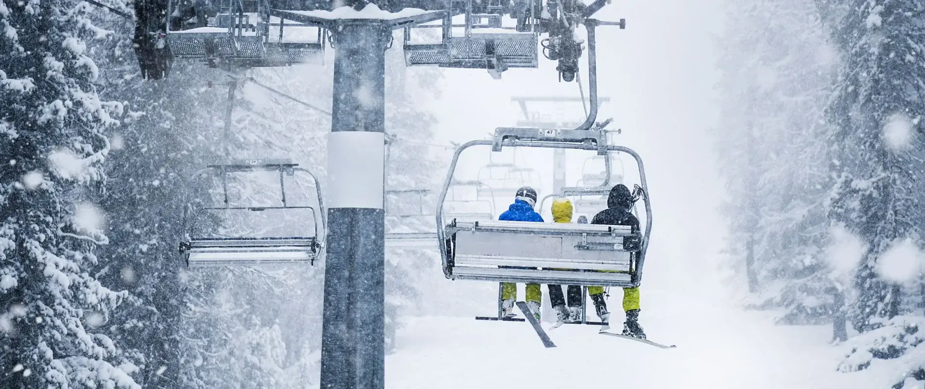 Three skiers on ski lift in heavy snowing storm. Beautiful vacation in winter mountains.