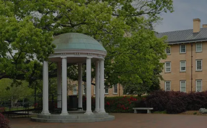 white gazebo with tree hanging over and brick building in background
