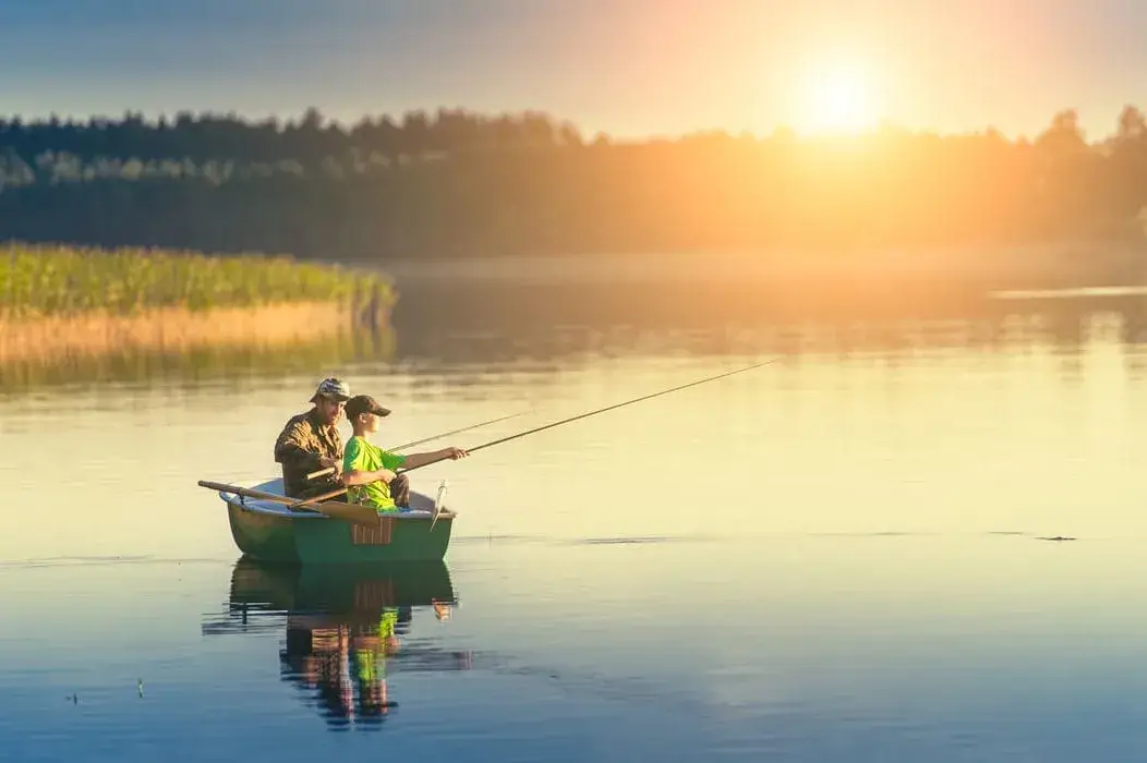 father and son catch fish from a boat at sunset