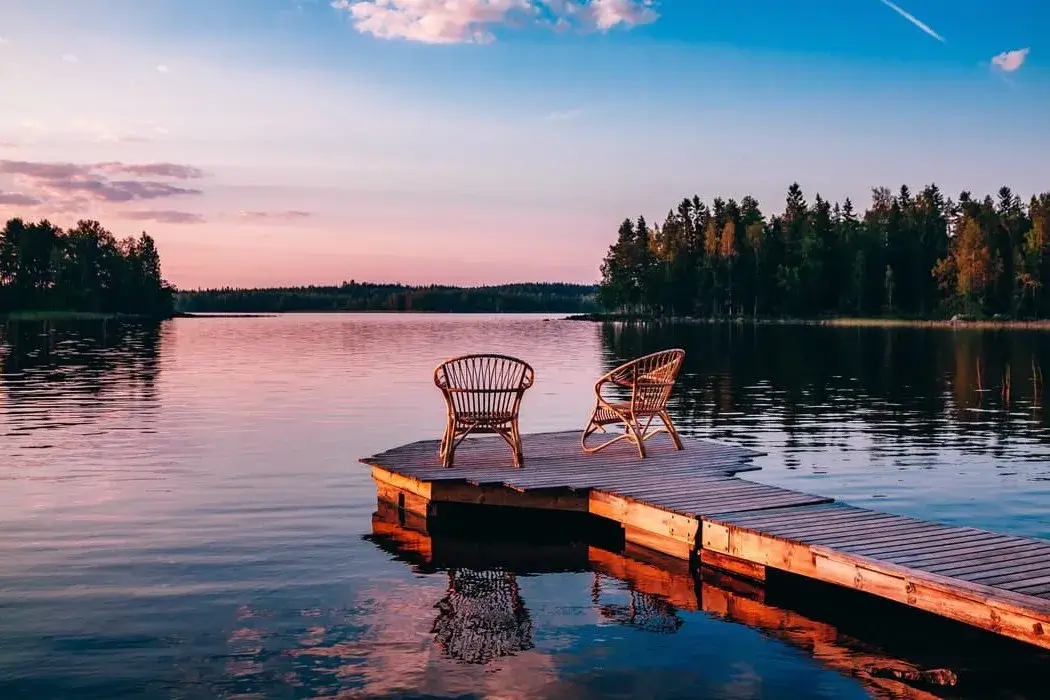 Two wooden chairs on a wood pier overlooking a lake at sunset