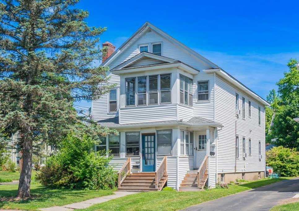 gray colored multi family building with lawn, trees and shrubbery