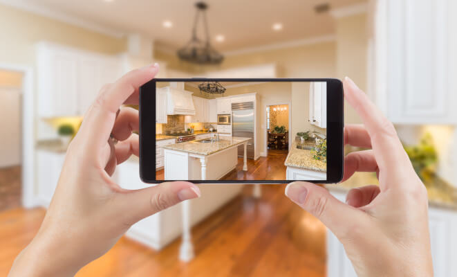 Female Hands Holding Smart Phone Displaying Photo of Kitchen Behind.
      