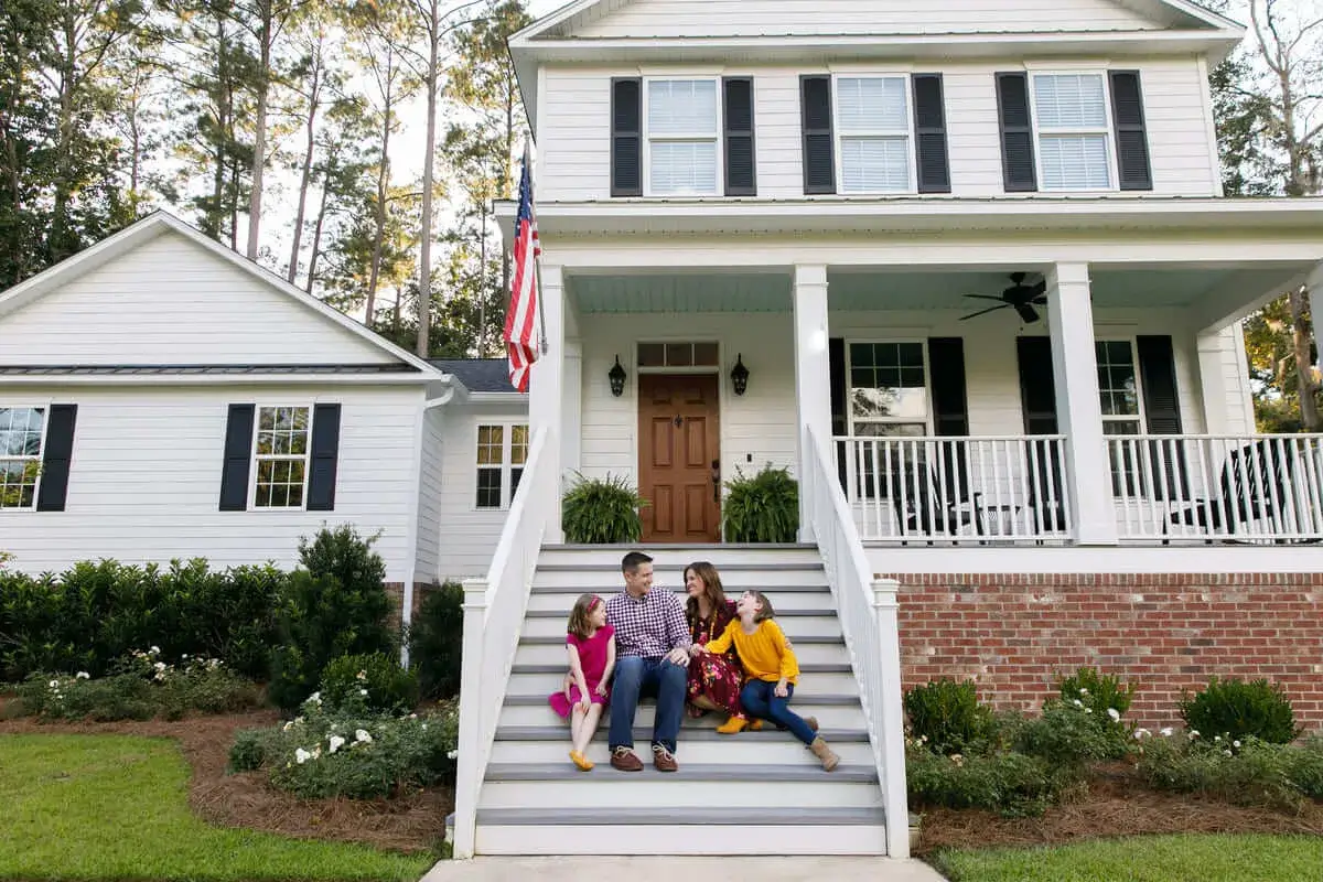 Family of Four With Daughters Sitting on the Steps Outside Their their Home Laughing Together