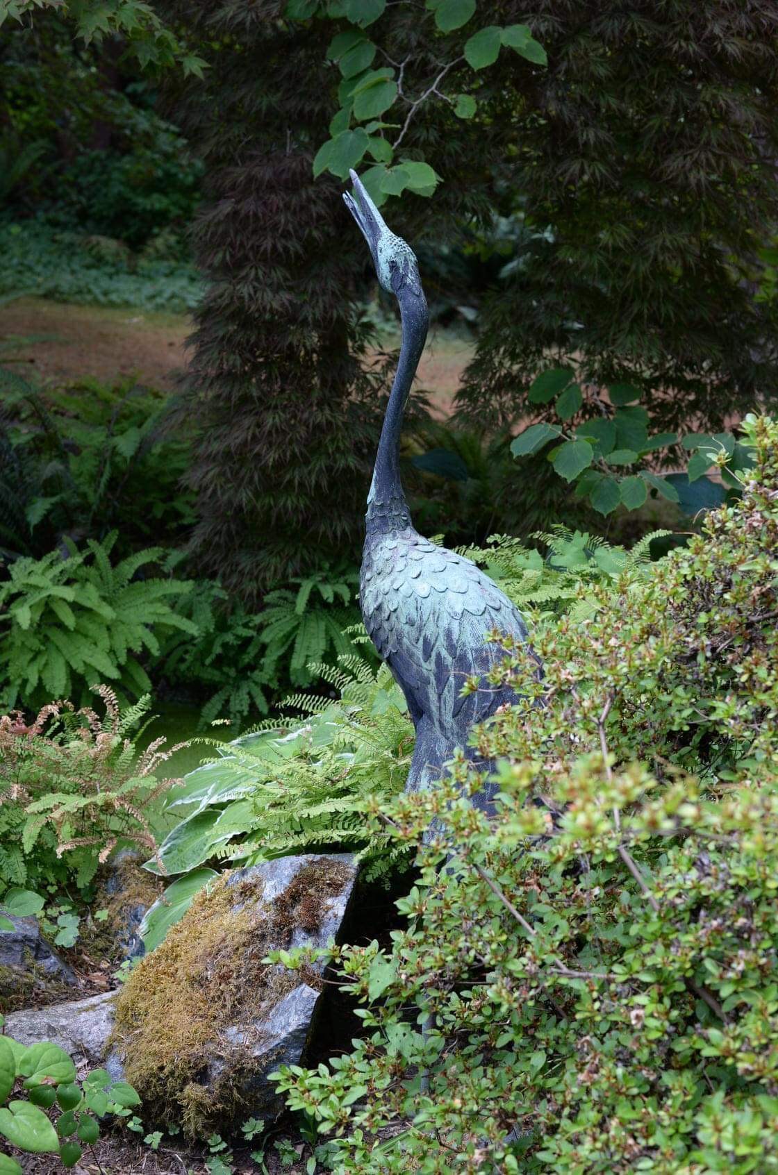 heron garden statue tucked between plants