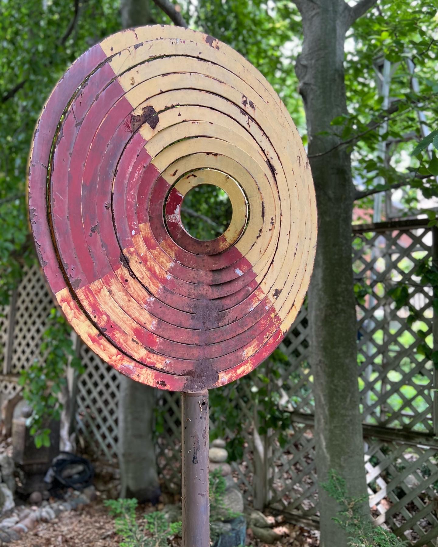 escultura de metal rojo y amarillo frente a árboles altos