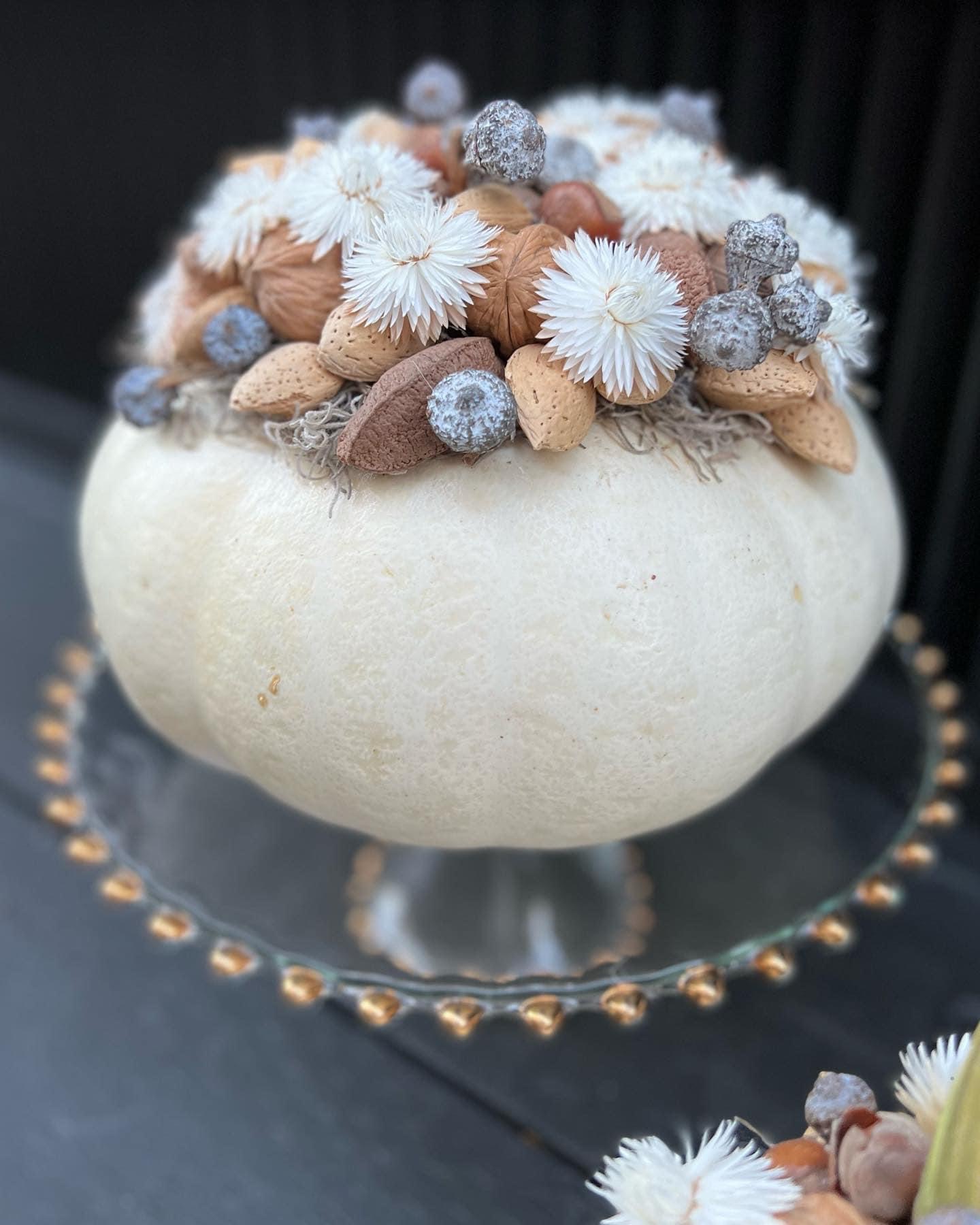 another small white pumpkin topped with mixed nuts and white strawflowers