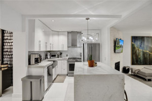 Open custom kitchen with gas stove top, Caesarstone quartz countertops and waterfall center island featuring bar seating