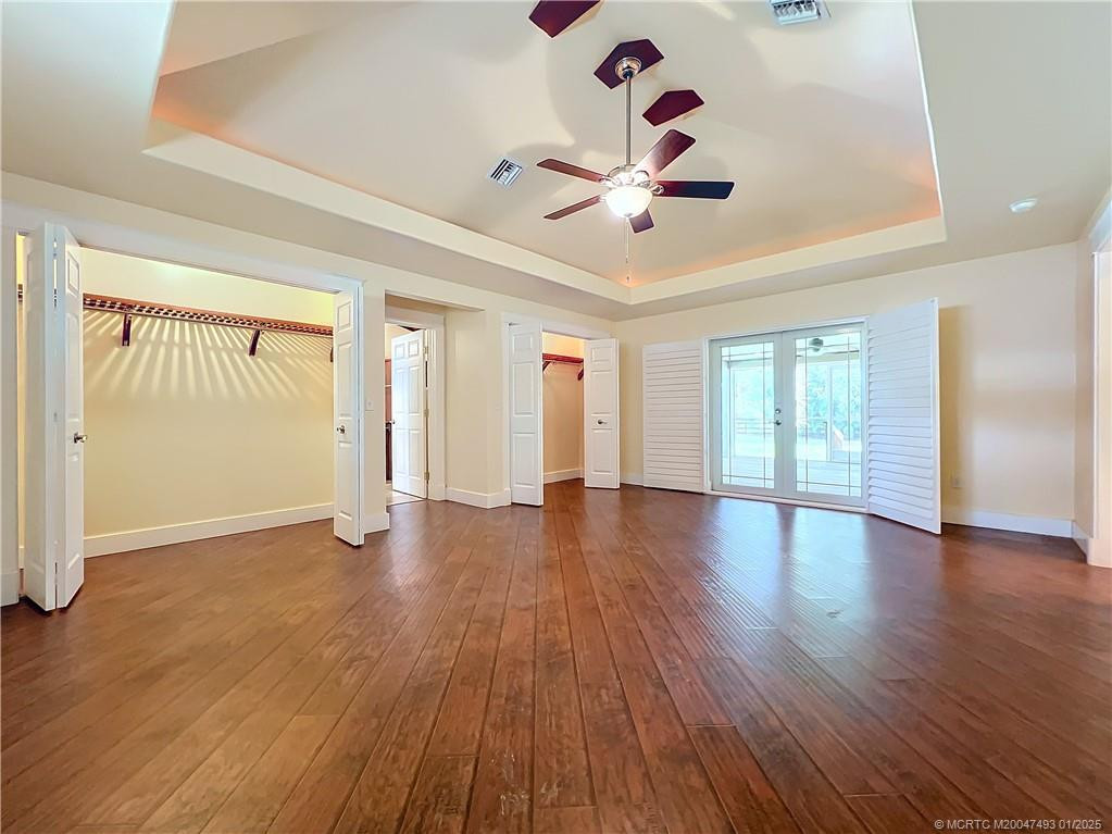 WOW ! look at this primary bedroom, laminate floors, impact French doors and window with plantation shutters, look up at the ceiling with a fan and flighting around the tray ceiling very high. middle door of the 2 closets is the primary bathroom. To the the left of the room is another window up high.